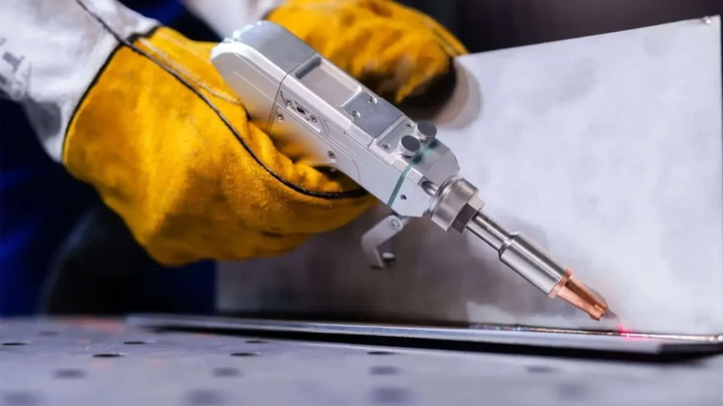 Operator w żółtych rękawicach ochronnych prowadzi precyzyjną głowicę laserową podczas procesu spawania lub obróbki krawędziowej na metalowym arkuszu.